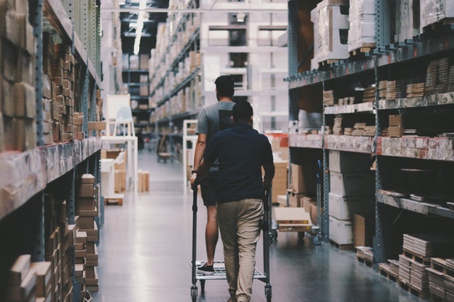 Warehouse worker walking down a long aisle between tall shelves with a cart