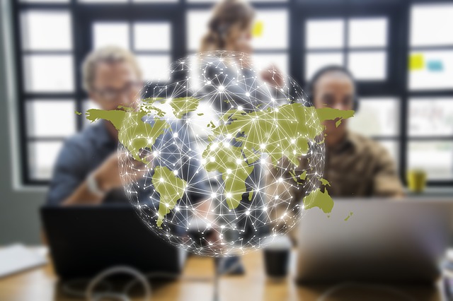 Three colleagues at laptops with a glowing world map overlaid on the scene