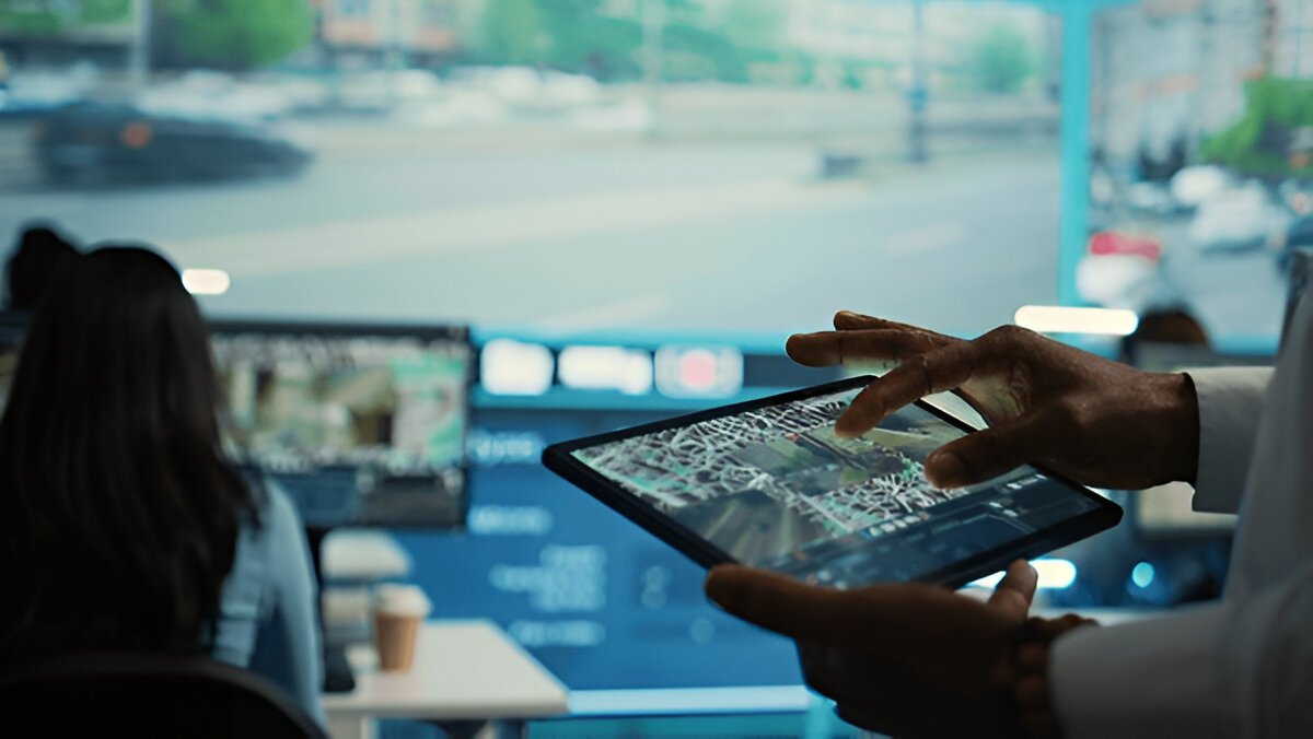 Person using a tablet showing a map in front of monitors in an operations room