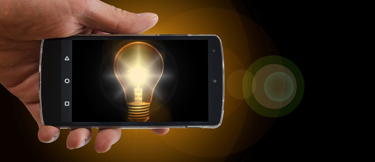 Hand holding a smartphone showing a glowing lightbulb