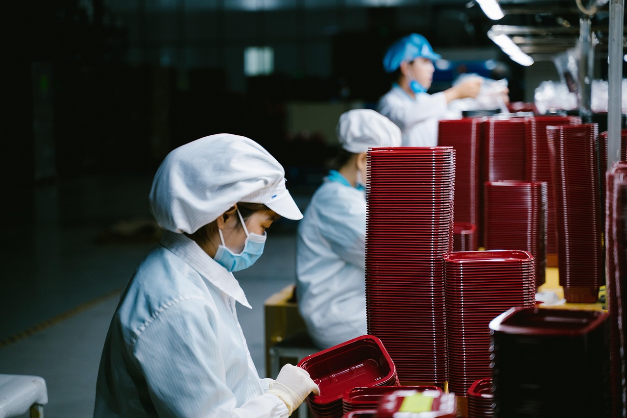 Workers in white caps and masks packing red trays on a factory production line